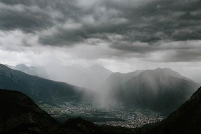 Photograph of town surrounded by mountains with clouds and rain above.